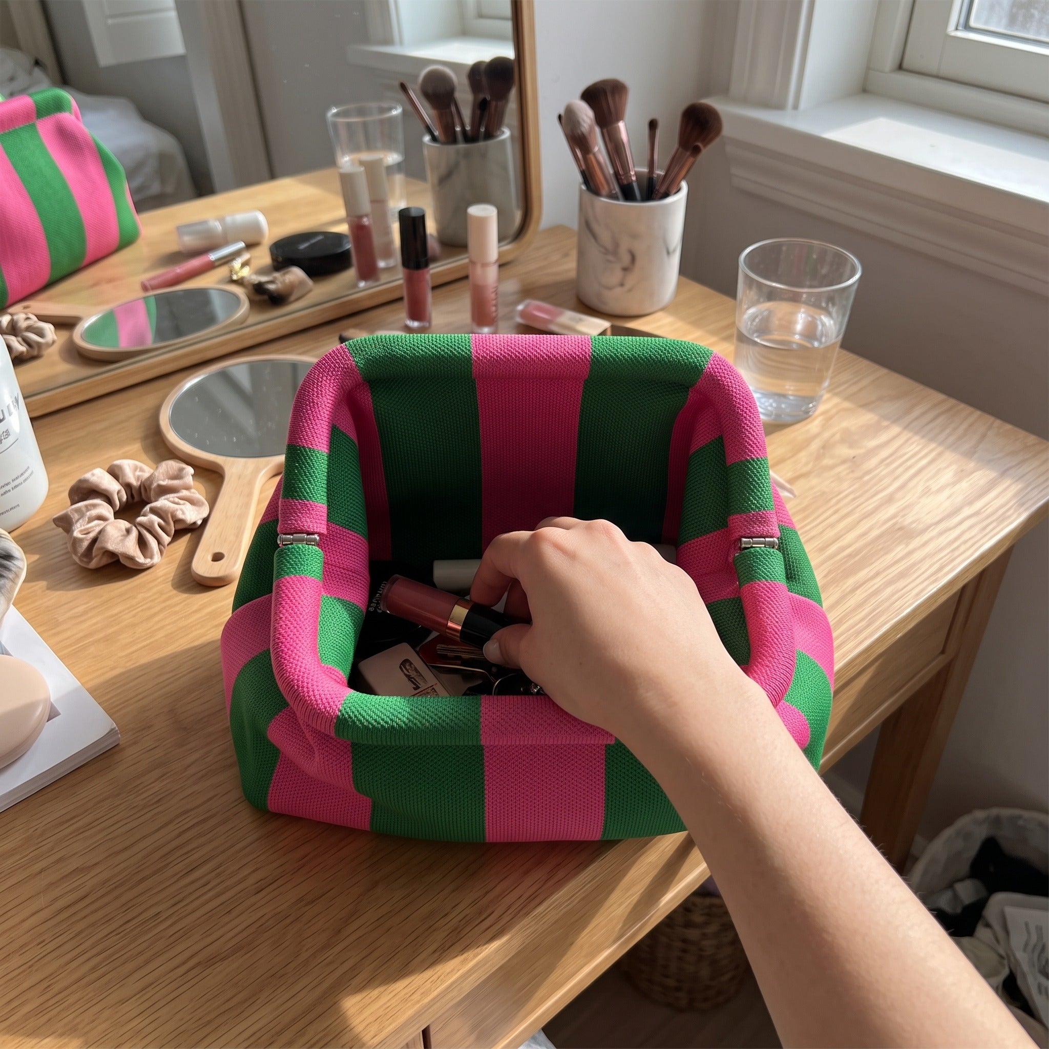 Hand reaching into green and pink Pop Pouch at a vanity