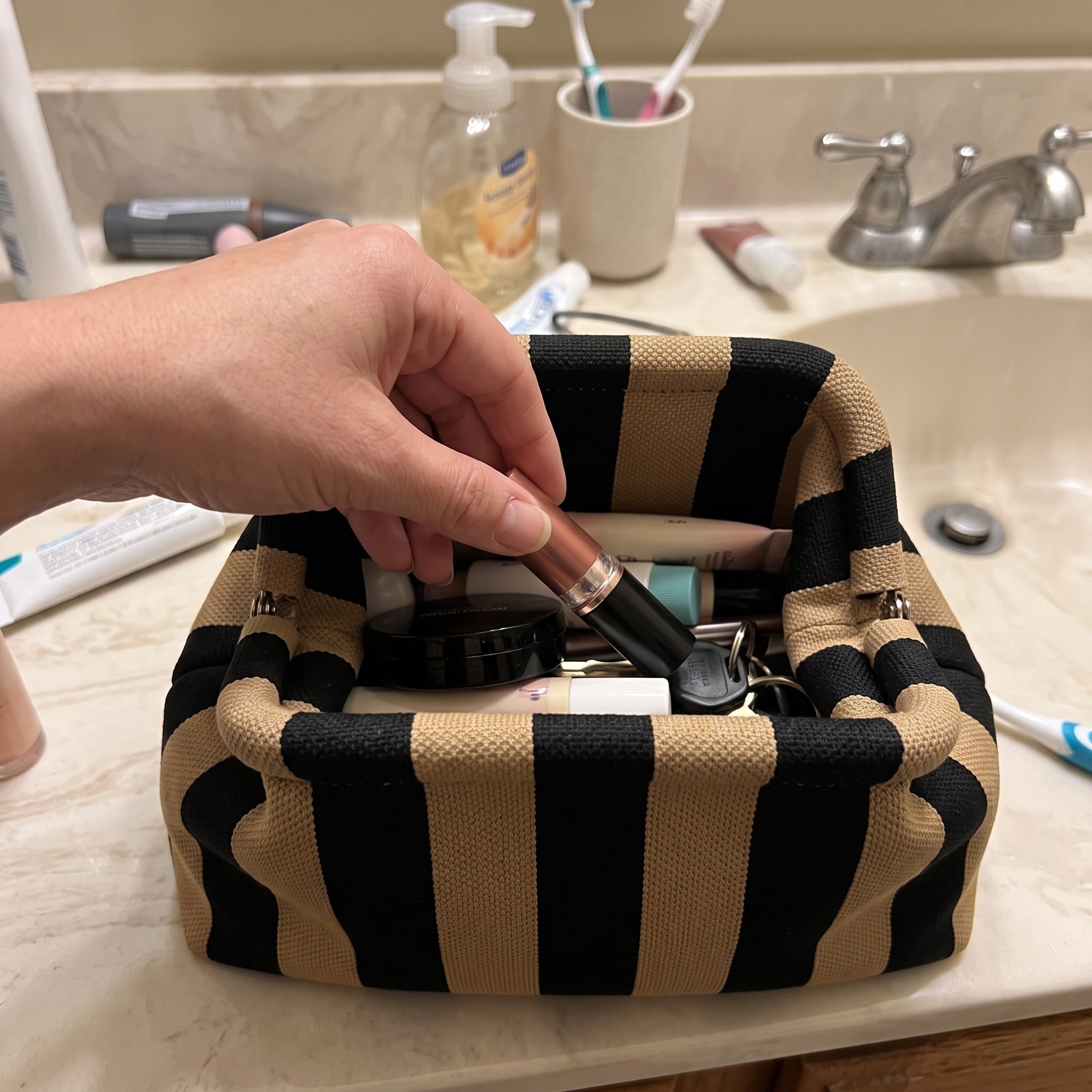 Hand choosing makeup from black and tan Pop Pouch